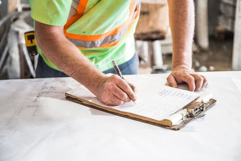 Construction worker writing on a clipboard beside drawings