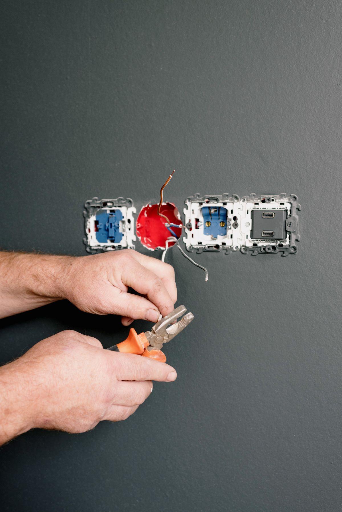 Electrician using pliers while working on an electrical outlet